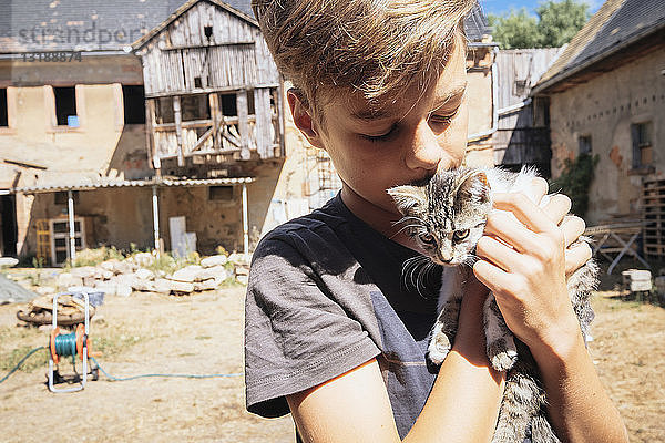 Anhänglicher Junge küsst Kätzchen auf sonnigem Bauernhof