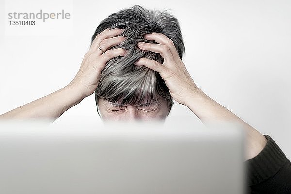 Gestresste Frau,  die hinter einem Computerbildschirm sitzt und an ihren Haaren zieht