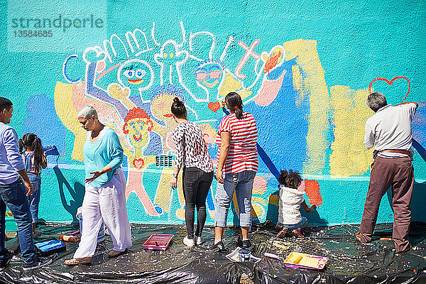 Freiwillige aus der Gemeinschaft malen ein lebendiges Wandgemälde an eine sonnige Wand