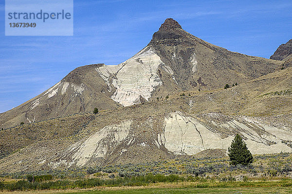 Sheep Rock shows various claystones of the John Day Group capped by resistant dark basalt layers of the Picture Gorge Group; viewed from the southwest; John Day Fossil Beds National Monument,  Oregon,  USA.