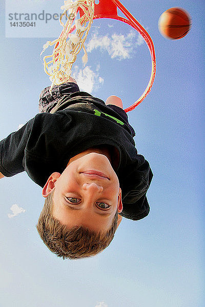 Boy Hanging from Basketball Hoop