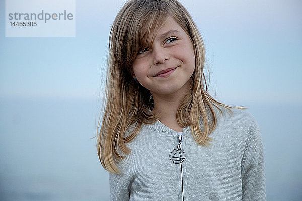 Porträt eines ausdrucksstarken,  hübschen kleinen Mädchens vor dem Meer bei Einbruch der Dunkelheit.