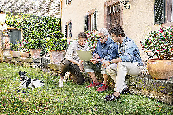 Drei Männer unterschiedlichen Alters sitzen mit Tablette im Garten