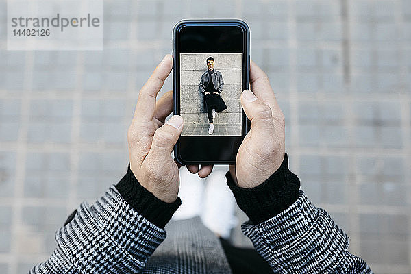 Mann hält Smartphone mit Foto von sich selbst in der Hand,  Nahaufnahme