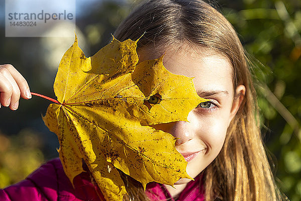 Porträt eines lächelnden Mädchens,  das durch ein Loch im Herbstblatt blickt