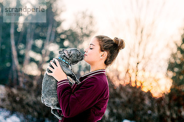 Mädchen küsst französischen Bulldoggenwelpen im Freien
