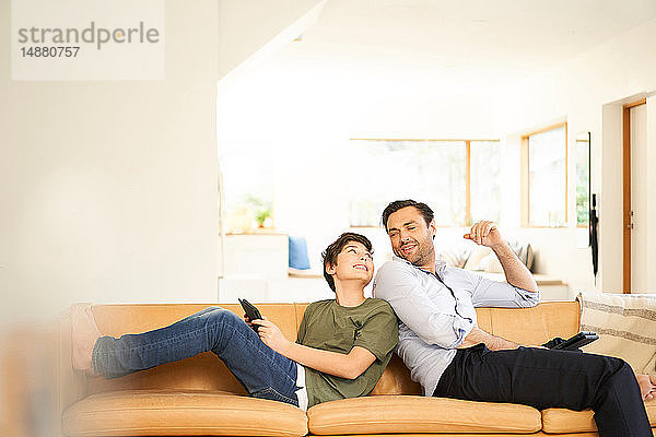 Junge und Vater benutzen digitale Tabletts Rücken an Rücken auf dem Sofa