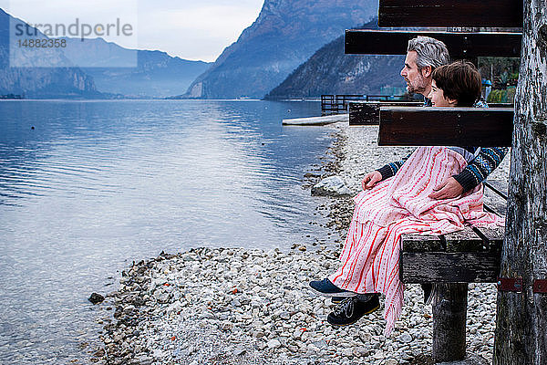 Junge und Vater eingewickelt in eine Decke am Seepier,  Seitenansicht,  Comer See,  Onno,  Lombardei,  Italien