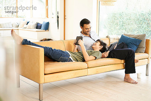 Junge und Vater benutzen digitale Tablets beim Entspannen auf dem Sofa