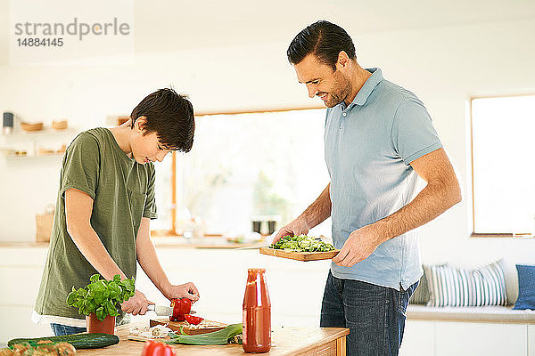 Junge schneidet rote Paprika an der Küchentheke,  Vater schaut zu