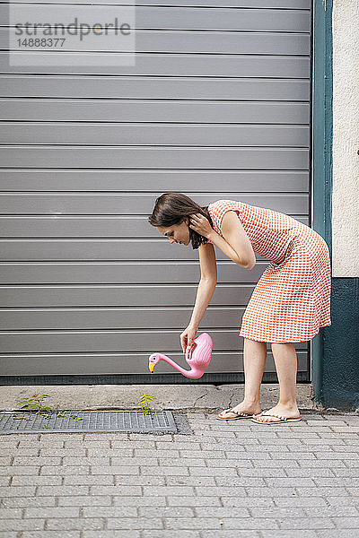 Frau gießt Pflanzen mit einer Flamingokanne in einer städtischen Straße