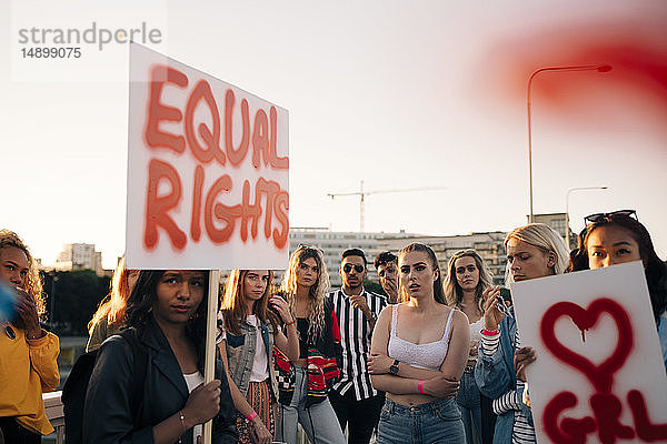Frauen und Männer mit Plakaten,  die für gleiche Rechte gegen den Himmel in der Stadt protestieren