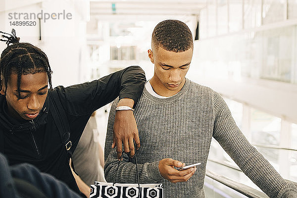 Teenager,  der ein Mobiltelefon benutzt,  während er einem Freund im Einkaufszentrum zur Seite steht