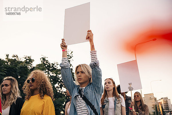 Junge Männer und Frauen protestieren mit Plakaten,  während sie in der Stadt gegen den Himmel marschieren