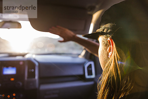 Frau als Beifahrerin auf dem Vordersitz eines Autos,  die die Augen vor Sonnenlicht schützt,  Blick über die Schulter