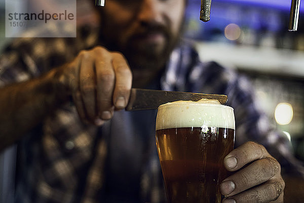 Mann mit Messer entfernt Schaum aus einem Bierglas