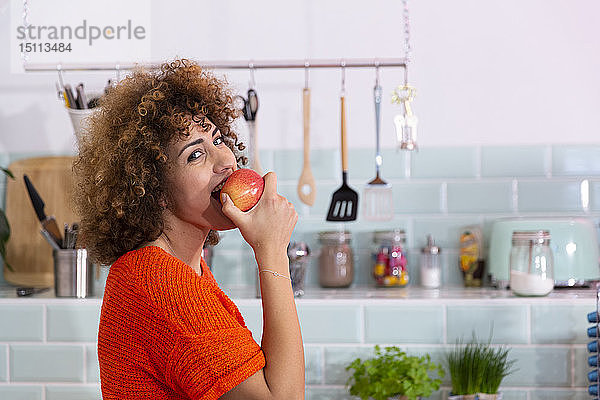 Porträt einer Frau,  die in einer Büroküche einen Apfel isst