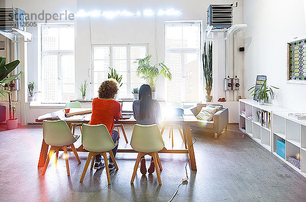 Rückansicht von zwei Frauen,  die in einem modernen Büro mit Videoprojektor auf dem Tisch arbeiten