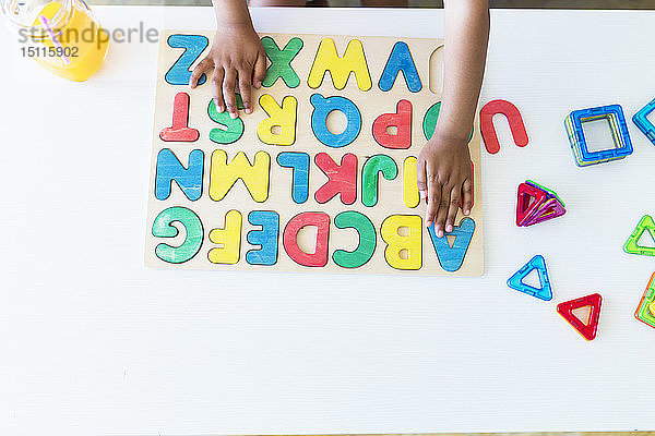 Nahaufnahme eines Mädchens,  das mit einem Alphabet-Lernspiel auf dem Tisch spielt