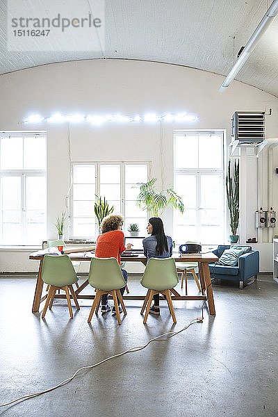 Rückansicht von zwei Frauen,  die am Tisch in einem modernen Büro arbeiten