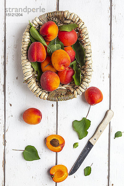Aprikosen im Korb,  Messer auf weißem Holz