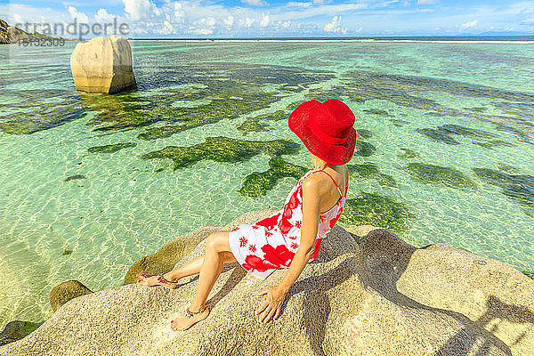 Touristin mit rotem Hut auf einem Granitfelsen an der Anse Source d'Argent,  Insel La Digue,  Seychellen,  Indischer Ozean,  Afrika
