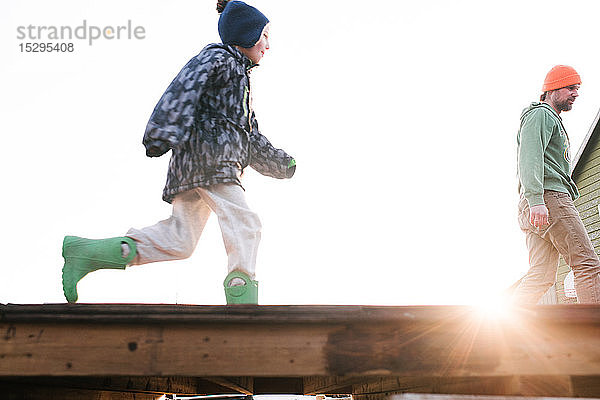 Junge mit Vater läuft über die sonnenbeschienene Skateboard-Rampe,  Blickwinkel niedrig