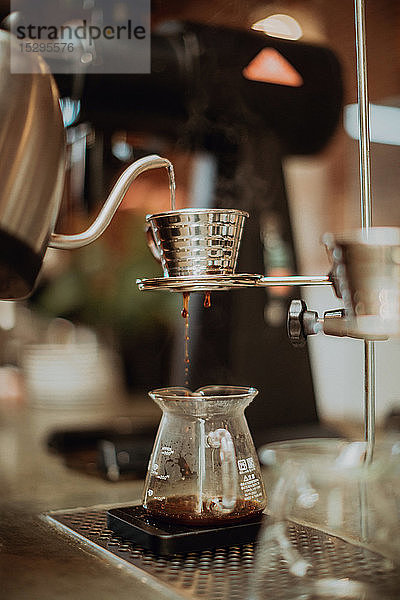 Gekochtes Kesselwasser,  das in den Kaffeefilter läuft und in die Kanne auf der Kaffeetheke tropft,  flacher Fokus