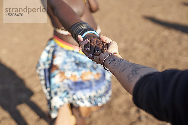 Traditionelle Muhacaona-Frau und weiße Frau halten Händchen,  Oncocua,  Angola