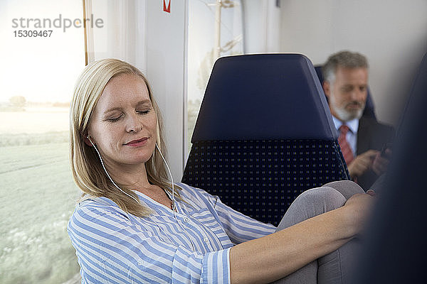 Frau sitzt in einem Zug und hört Musik mit Kopfhörern