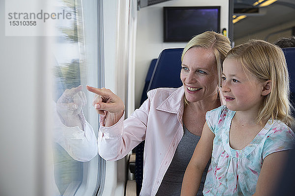 Mutter und Tochter reisen mit dem Zug und zeigen aus dem Fenster