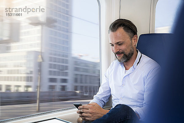 Älterer Mann sitzt in einem Zug und benutzt ein Smartphone