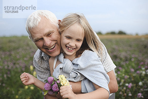 Porträt eines glücklichen Grossvaters und einer glücklichen Enkelin mit gepflückten Blumen auf einer Wiese