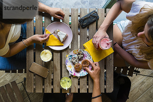 Draufsicht auf drei junge Frauen,  die an einem Holztisch mit Smoothies und Keksen sitzen