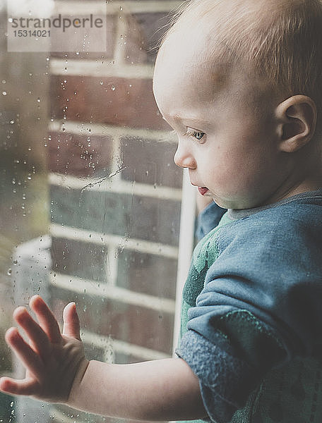 Kleines Mädchen schaut durch ein mit Regentropfen bedecktes Fenster