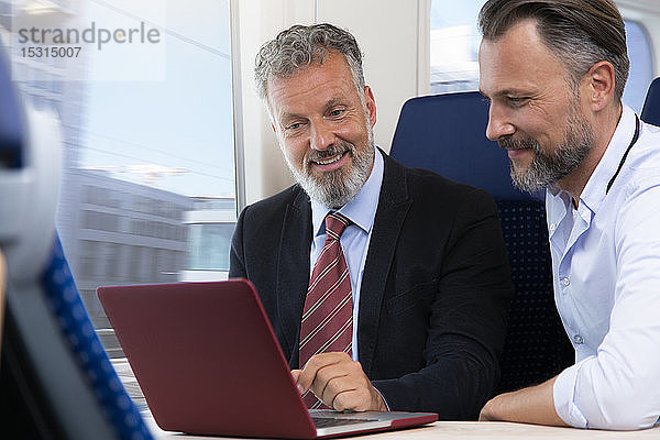Geschäftsleute,  die mit dem Zug reisen und am Laptop arbeiten