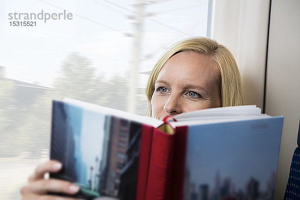 Frau sitzt im Zug und liest Buch