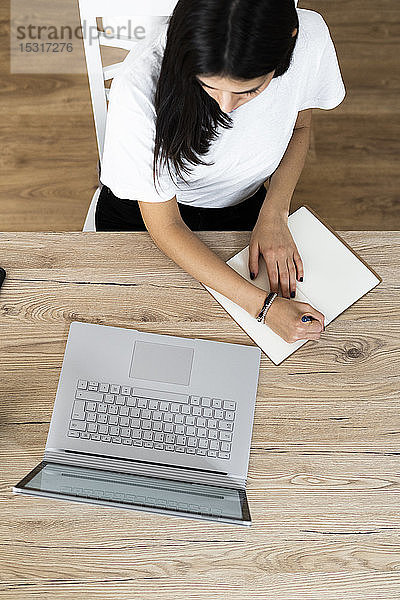 Draufsicht einer jungen Frau mit Laptop,  die Notizen macht
