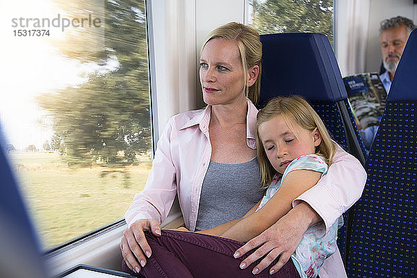 Tochter schläft auf dem Schoß der Mutter in einem Zug