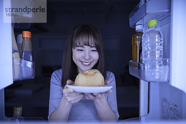 Junge Japanerin isst Nachtsnack aus dem Kühlschrank