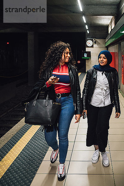 Junge Frau im Hidschab mit Freundin auf U-Bahn-Bahnsteig