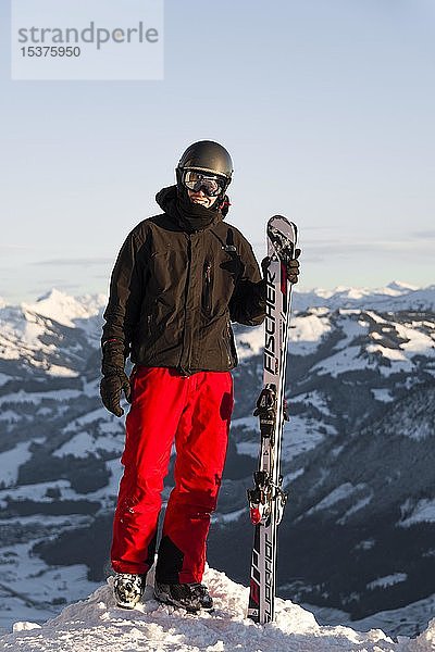 Skifahrer steht an der Piste und hält Ski,  Blick in die Kamera,  Gipfel Hohe Salve,  SkiWelt Wilder Kaiser Brixenthal,  Hochbrixen,  Tirol,  Österreich,  Europa
