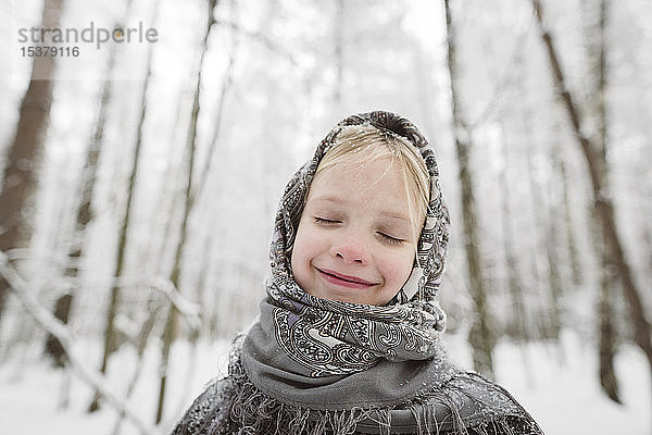 Porträt eines glücklichen kleinen Mädchens mit Kopftuch im Winterwald