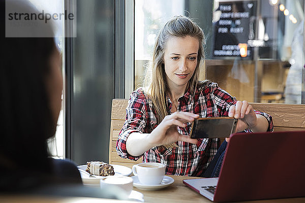 Frau benutzt Handy und Laptop in einem Café