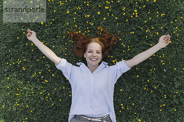 Porträt einer glücklichen rothaarigen Frau,  die auf einer Blumenwiese liegt