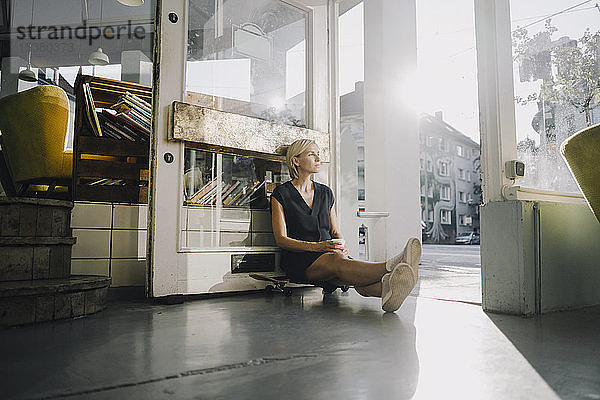Geschäftsfrau im Café,  sitzt auf einem Skateboard und entspannt