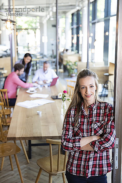 Porträt einer ungezwungenen Geschäftsfrau in einem Cafe mit Kollegen,  die im Hintergrund eine Besprechung abhalten