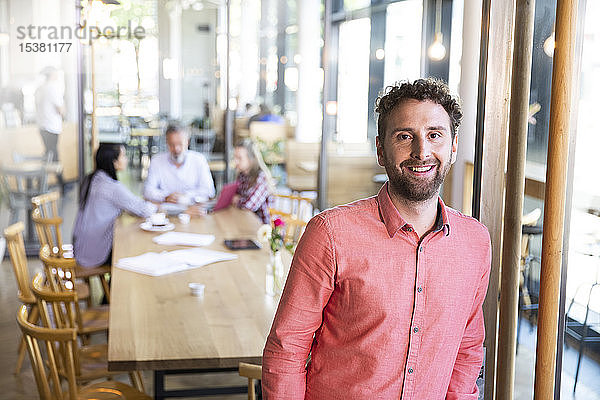 Porträt eines Gelegenheits-Geschäftsmannes in einem Cafe mit Kollegen,  die im Hintergrund ein Treffen haben