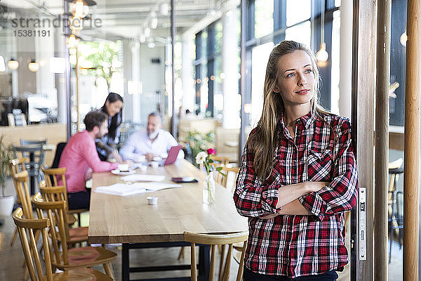 Porträt einer ungezwungenen Geschäftsfrau in einem Cafe mit Kollegen,  die im Hintergrund eine Besprechung abhalten