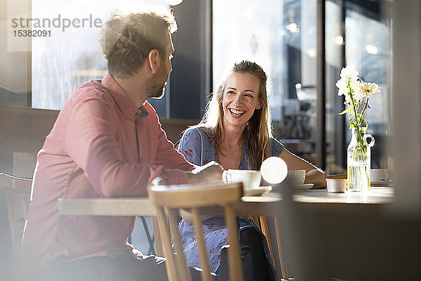 Lachende Frau und lachender Mann unterhalten sich am Tisch in einem Cafe